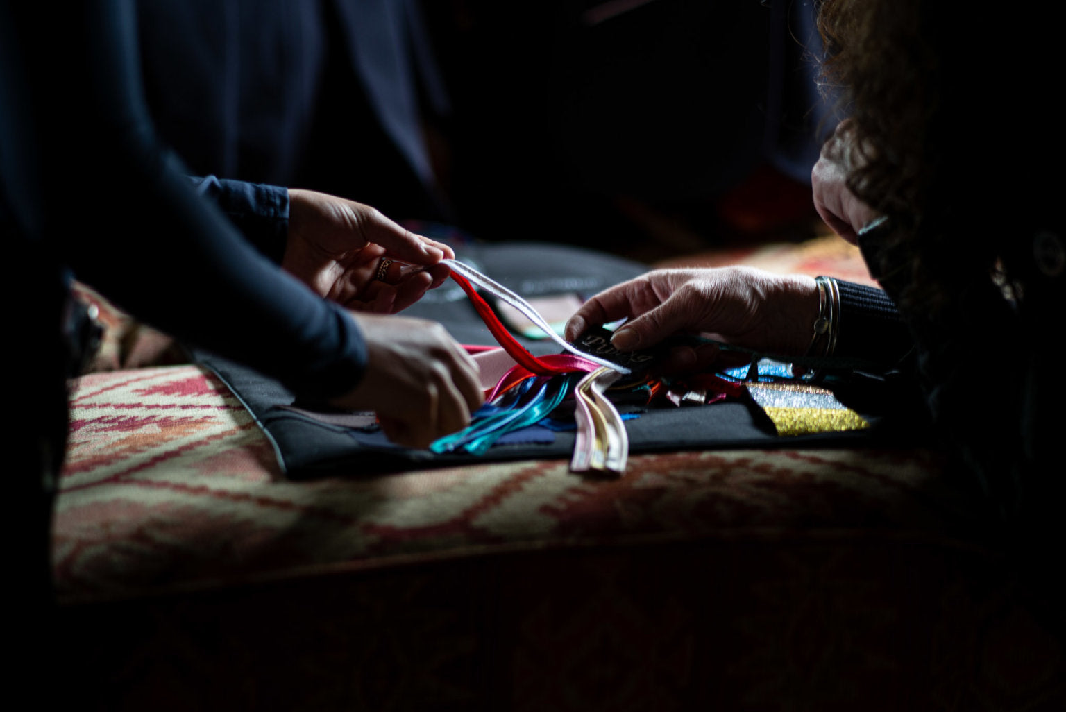 Two people working with colorful fabric on a dark background
