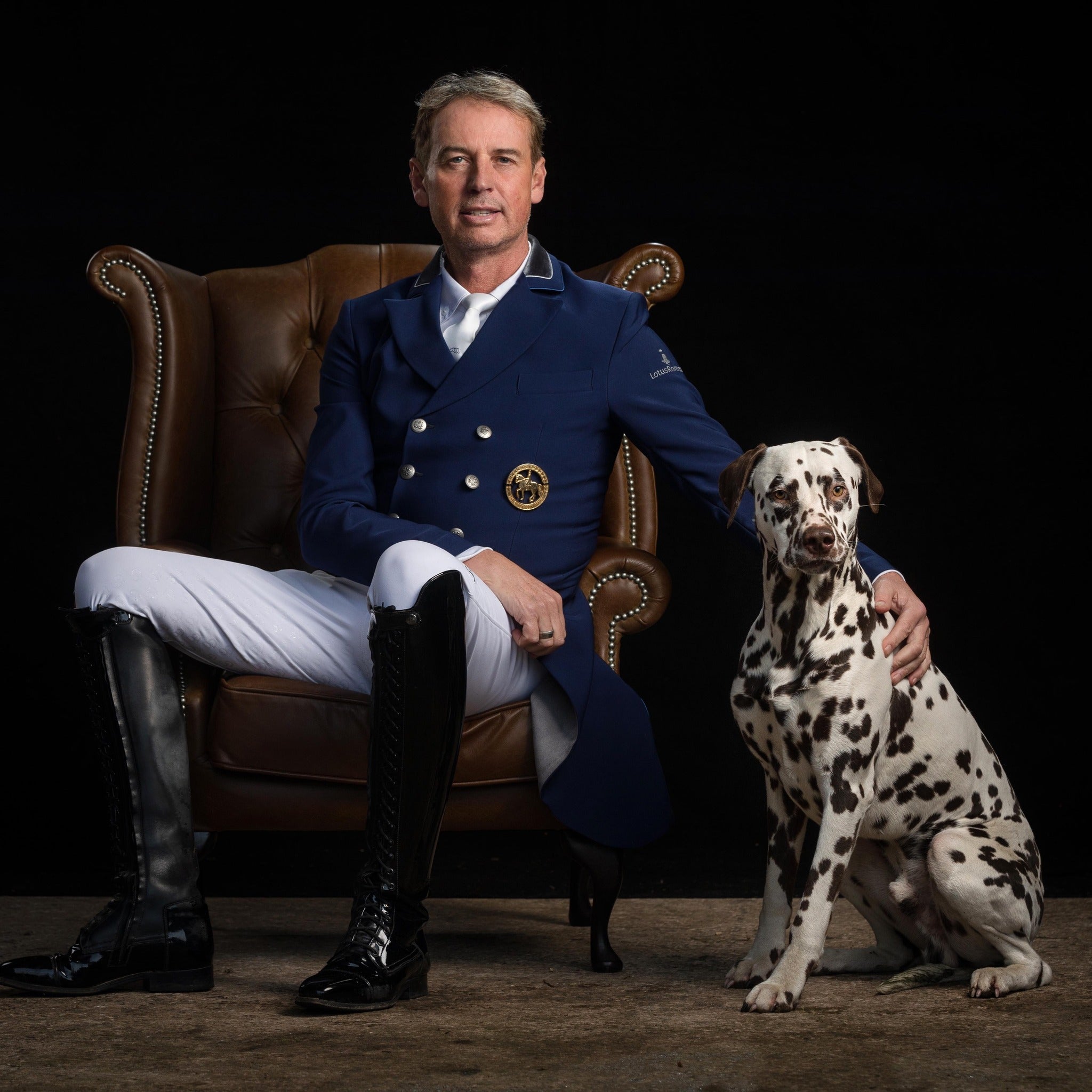 CARL HESTER in equestrian attire sitting on a leather chair with a Dalmatian dog.